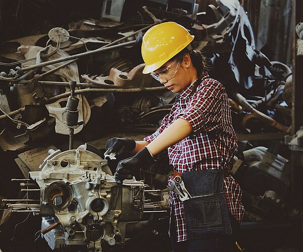 Frau mit gelbem Helm arbeitet an einer Maschine