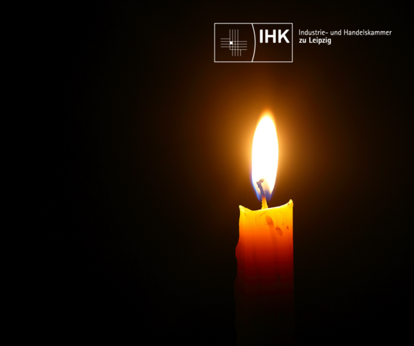 Eine brennende Kerze in der Dunkelheit, darüber das Logo der IHK zu Leipzig