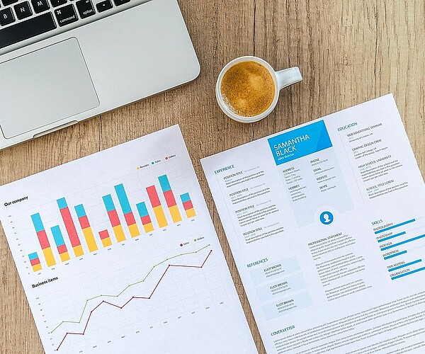 Statistiken auf Papier neben Rechner und Kaffeetasse