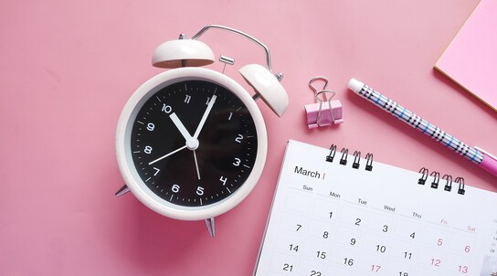 analoge Uhr liegt neben Kalender 