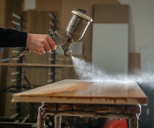 Mann sprüht Holzschutz auf Holzplatte