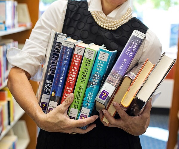 Mann trägt viele Bücher in der Bibliothek mit sich herum
