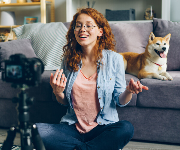 Beautiful blogger and cute dog recording video using camera at home talking