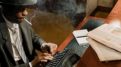 Krimilounge: Mann raucht und tippt auf einer altmodischen Schreibmaschine