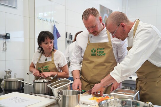 Gemüse schneiden | © Speiseräume Gemüse schneiden im Kochworkshop: drei Menschen schnippeln Paprika in Stadt-Land-Küche-Schürzen