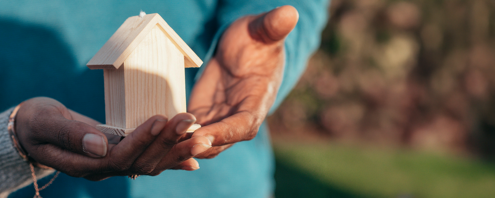 Zwei Hände halten ein Holzhäuschen schützend fest